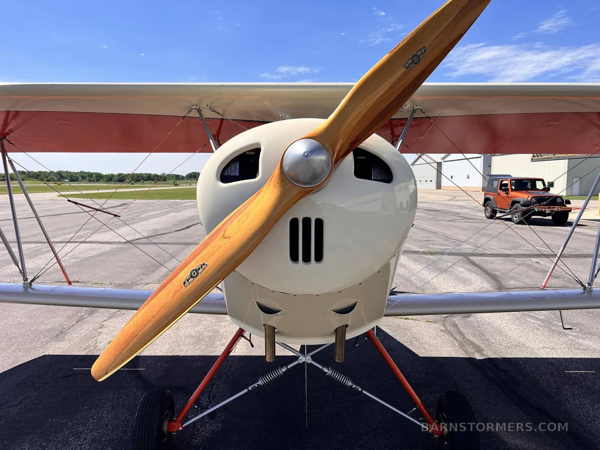 A head-on view of the red and white biplane, highlighting its wooden propeller and engine cowling.