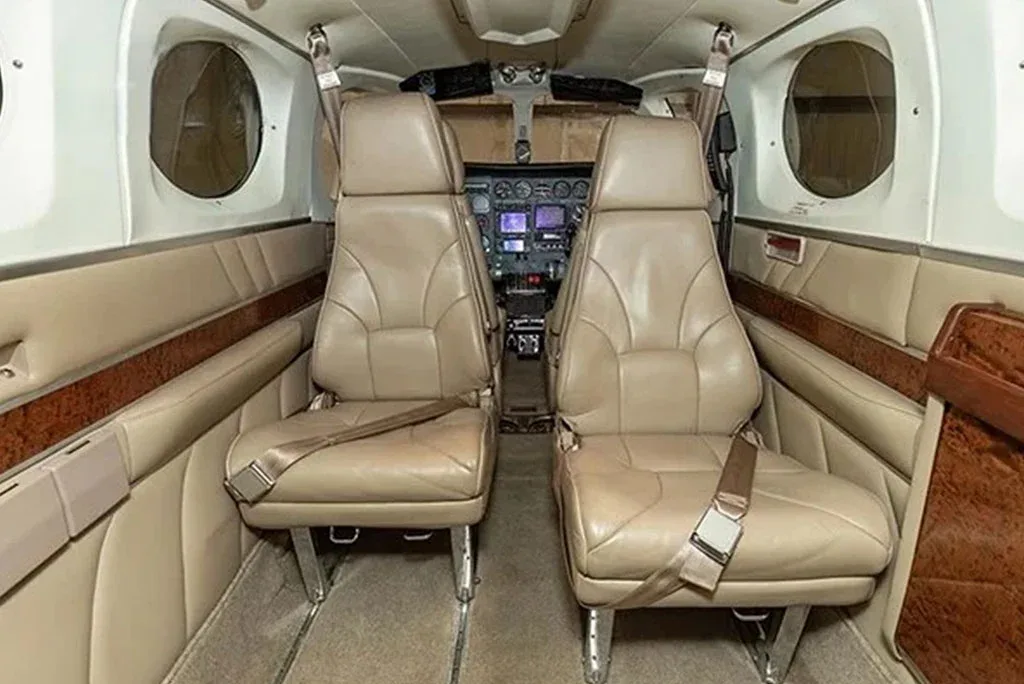 The aircraft's interior cabin with two tan leather passenger seats, with a glimpse of the cockpit in the background.