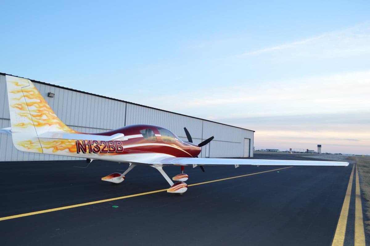 The aircraft is parked on the tarmac with a hangar and control tower in the background.