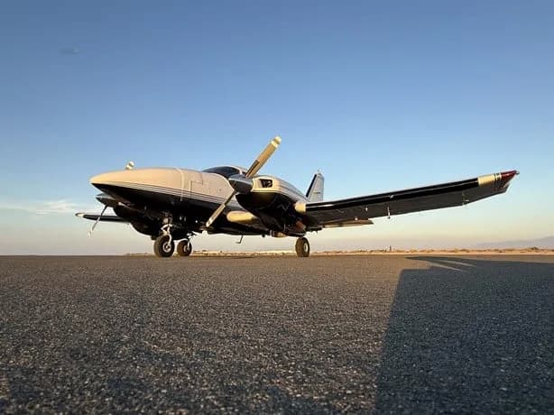 A low-angle view of a silver and black single-engine aircraft parked on an asphalt runway under a clear sky.