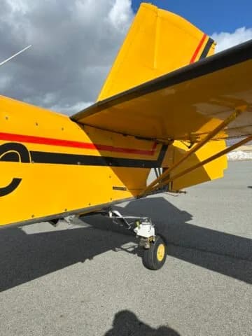 Close-up view of the tail wheel and lower tail section of a yellow crop duster aircraft.