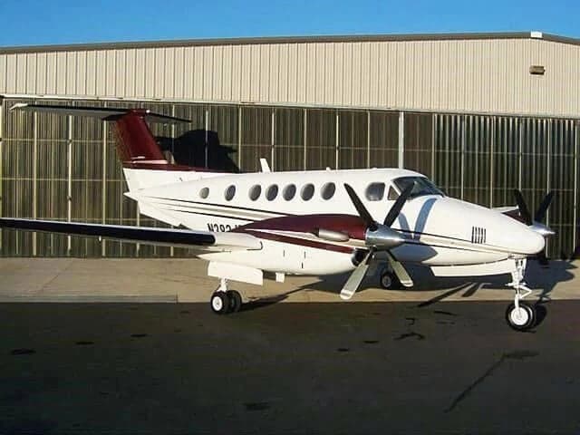A white and maroon Beechcraft King Air parked on the tarmac outside a hangar.