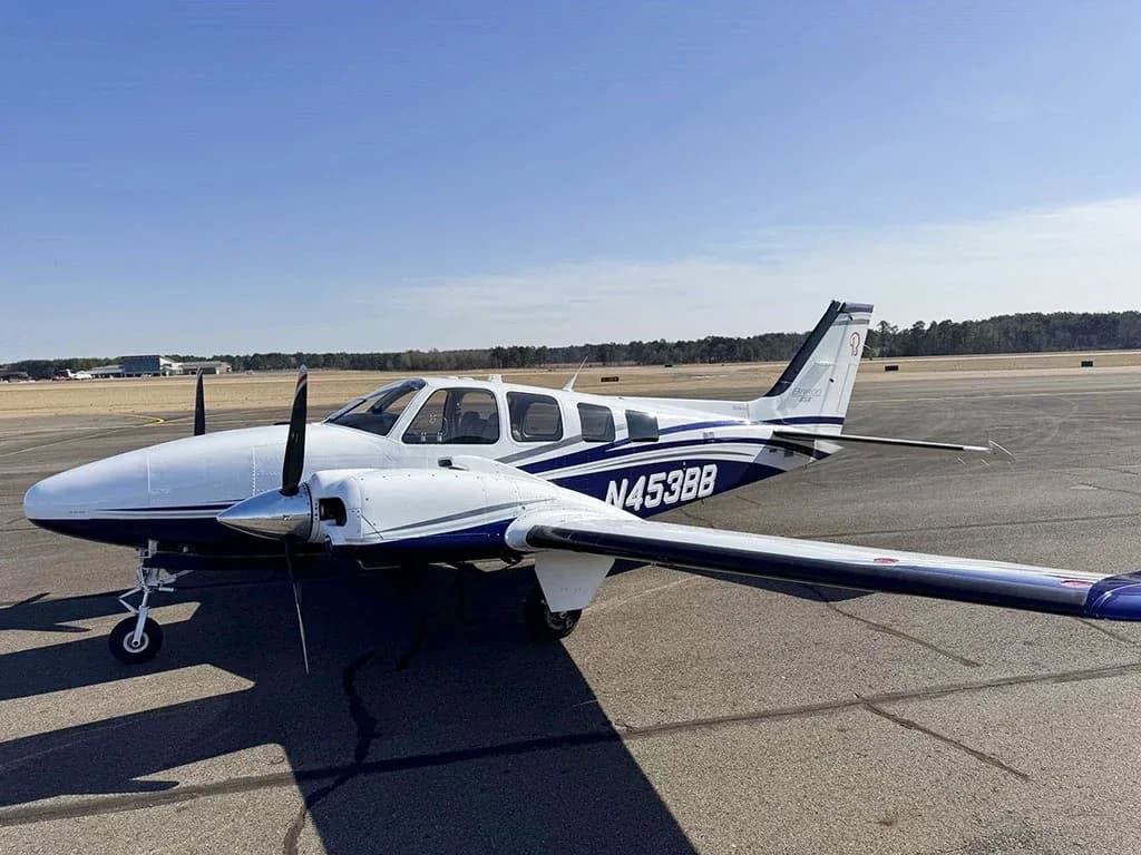 A white and blue Beechcraft Baron N453BB parked on an airfield, viewed from the front-right.