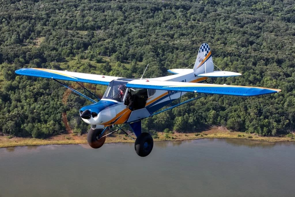 Aircraft flying over a body of water with a forest in the background.