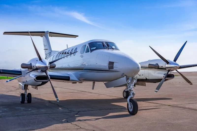 A white Beechcraft King Air 350i with tail number N725TR is parked on an airfield, viewed from the front-right.