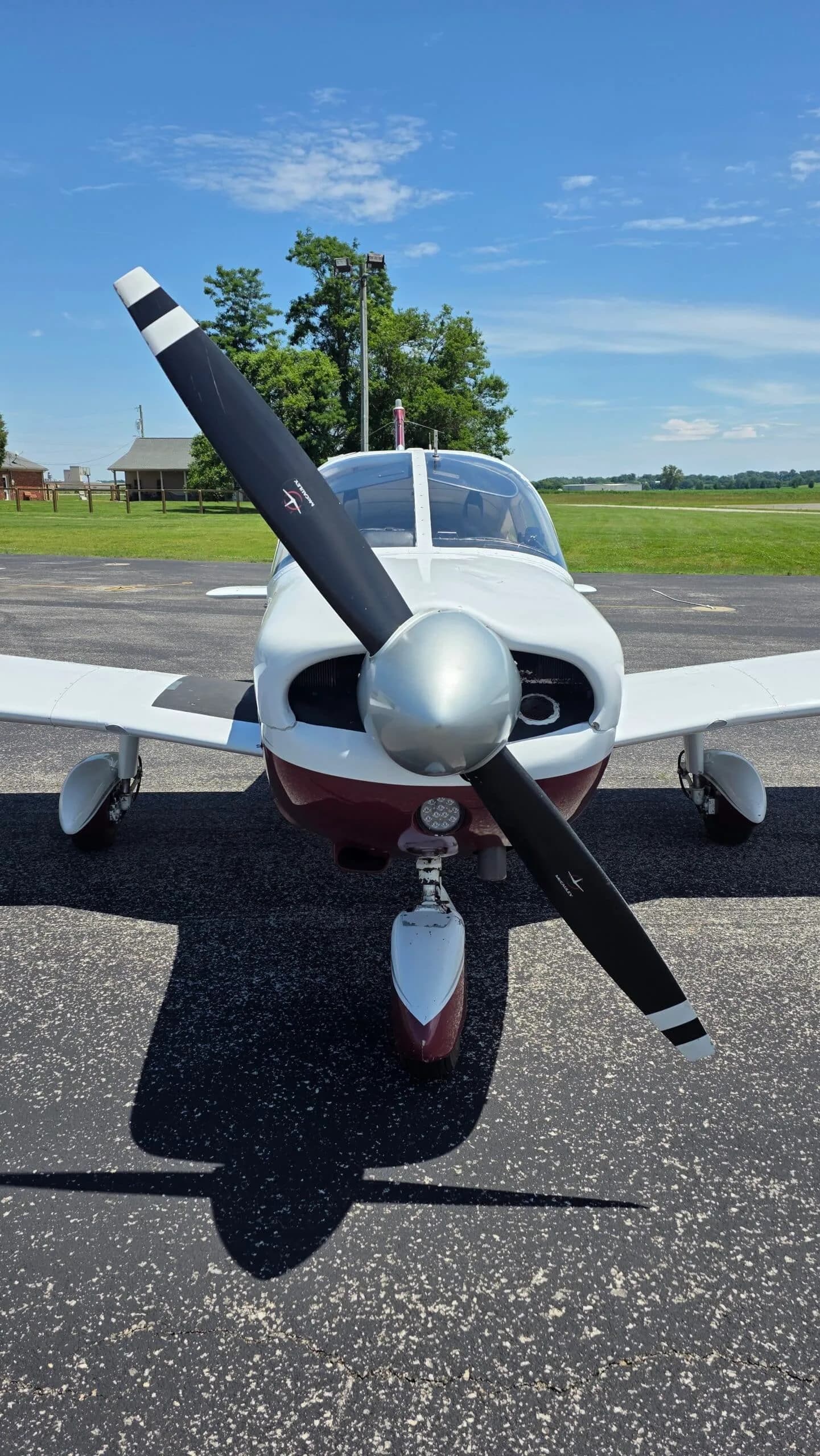 A close-up front view of the propeller and nose of a white and maroon Piper Cherokee (N9221W).