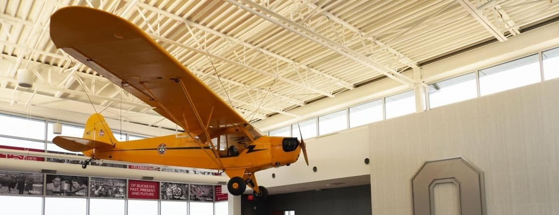 A yellow Piper Cub aircraft is suspended from the ceiling of a building.