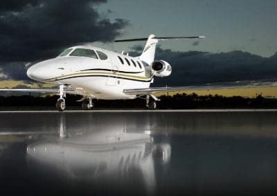 A Citation CJ3+ aircraft is parked on a reflective surface at sunset.