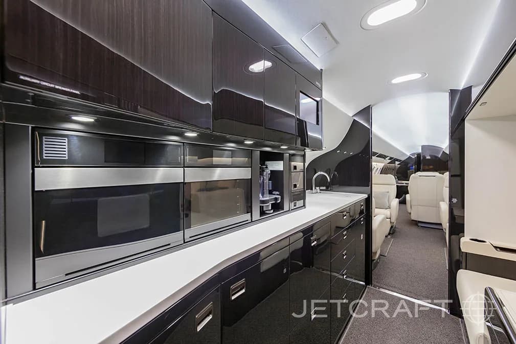 A luxurious aircraft galley with dark wood cabinetry, white countertops, and integrated appliances.