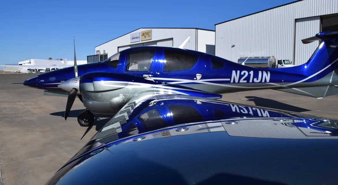 Side view of a Diamond DA62 aircraft with a blue and silver paint scheme, showing the registration N21JN.