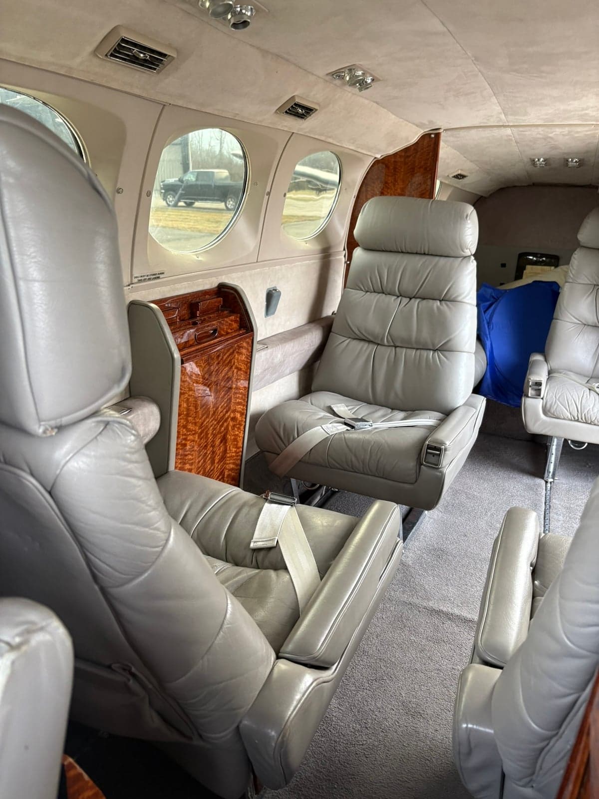 View of the aircraft cabin interior showing multiple grey leather seats and wood accents.