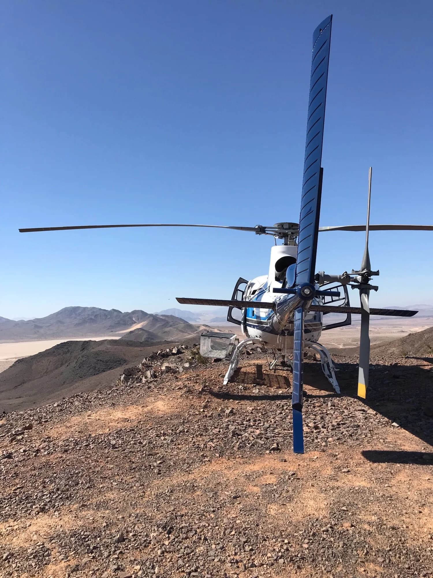 A helicopter sits on a rocky hilltop with mountains in the background.