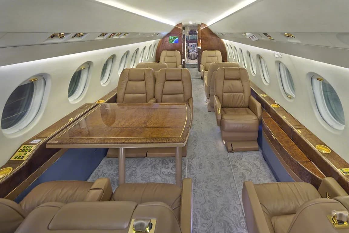 The spacious cabin interior of a private jet with tan leather seating and a large wooden table.