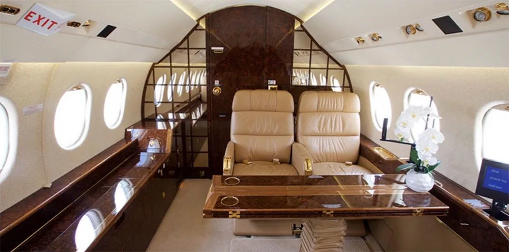 The elegant private jet cabin interior with tan leather seats, a polished wood table, and a white orchid.