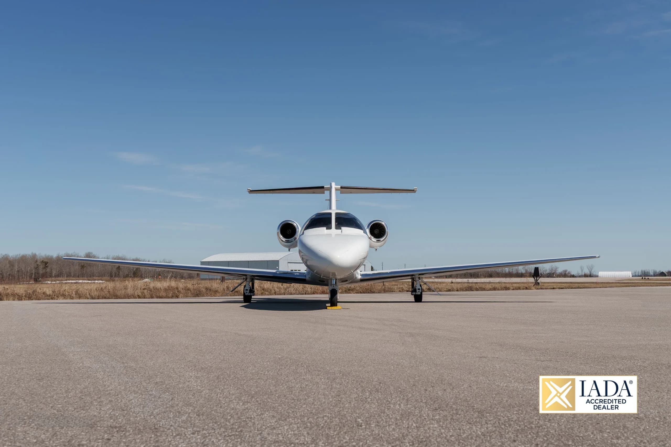 A white Cessna Citation business jet (N21RA) with red and blue stripes parked on an airfield, viewed head-on.