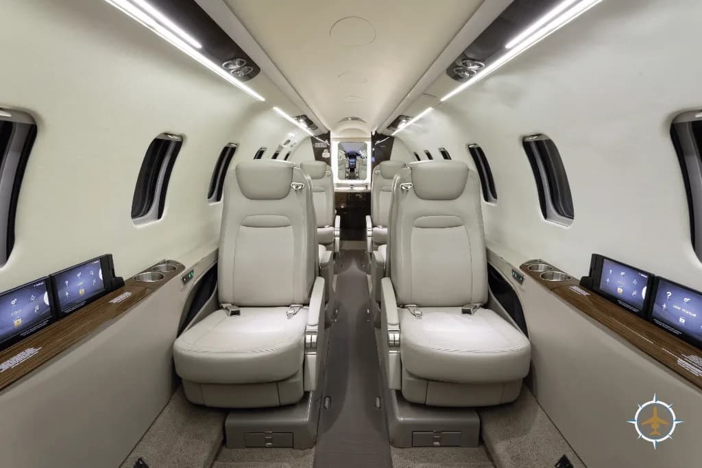 The spacious cabin interior of a business jet with light-colored leather seats and individual screens.