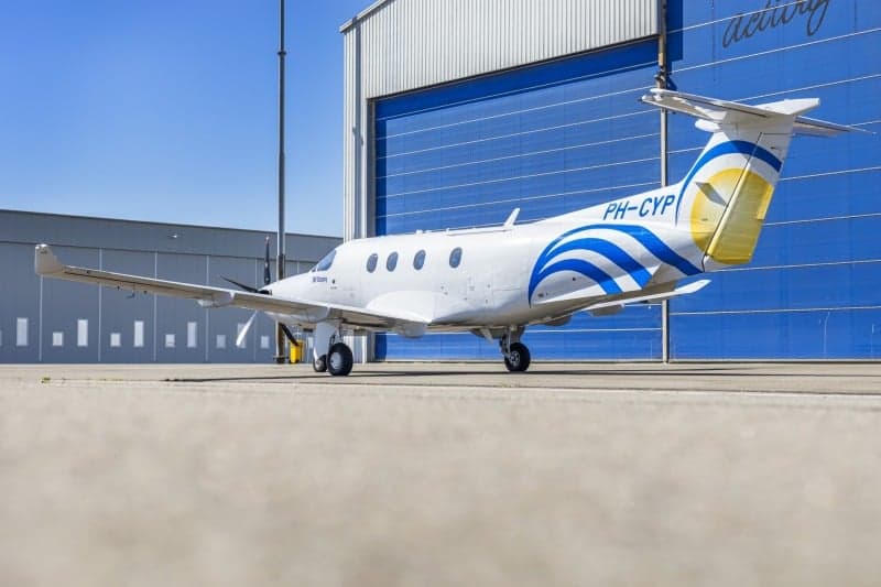 A Pilatus PC-12 aircraft with registration PH-CYP parked on the tarmac in front of a hangar, viewed from the rear.