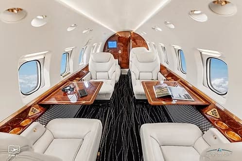 The interior of a jet aircraft with white leather seats and wood trim.
