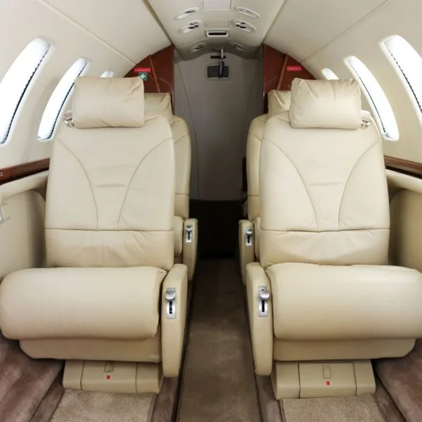 View down the aisle of a private jet cabin with light beige leather seats and wood trim.