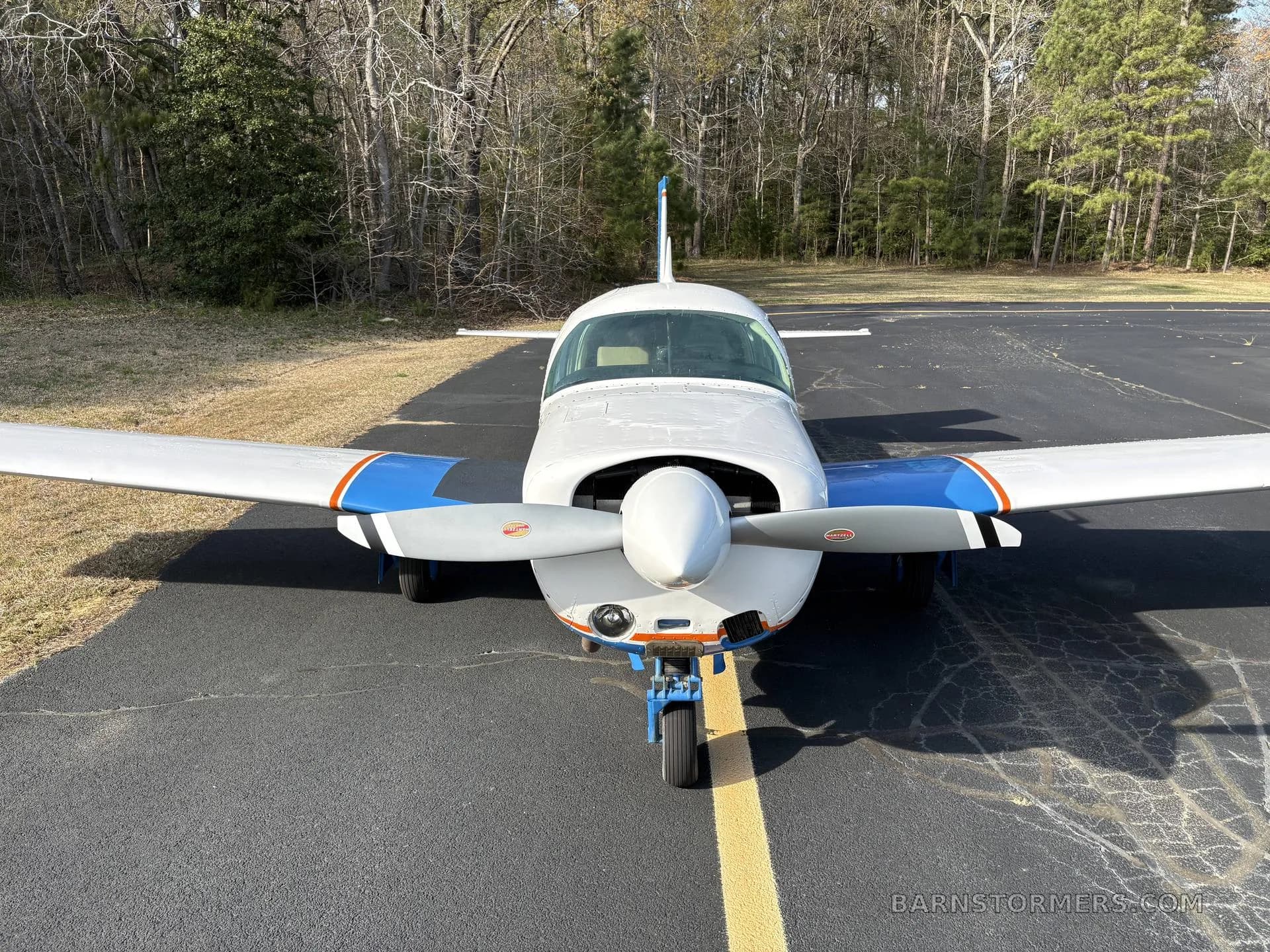 A front view of a white and blue single-engine aircraft with tail number N46EC parked on an asphalt runway.