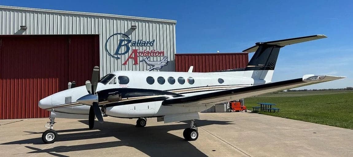 King Air aircraft with white and black paint scheme parked in front of a hangar.