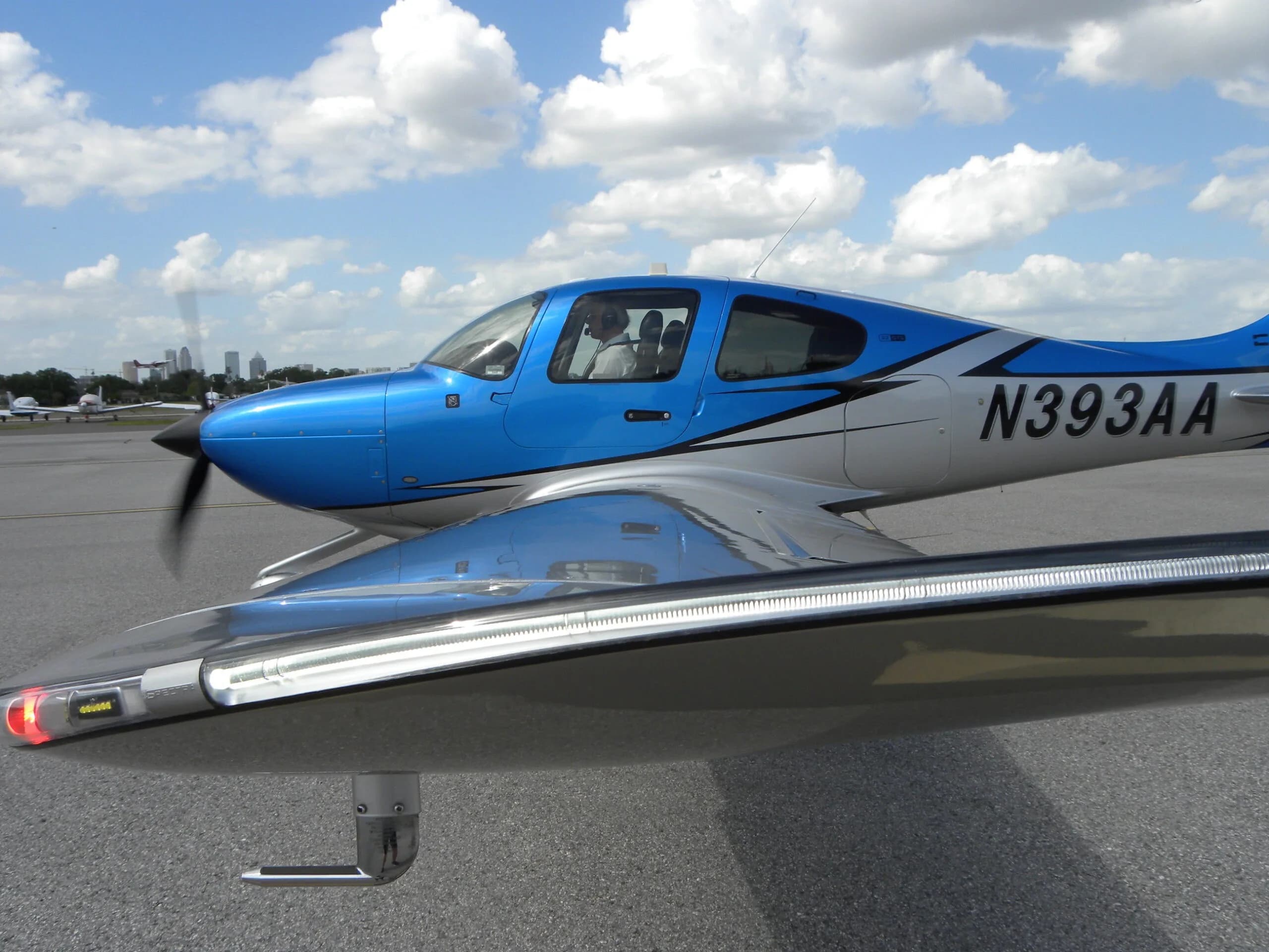 A side view of a blue and silver Cirrus SR22 aircraft with registration N393AA, showing the wingtip light.