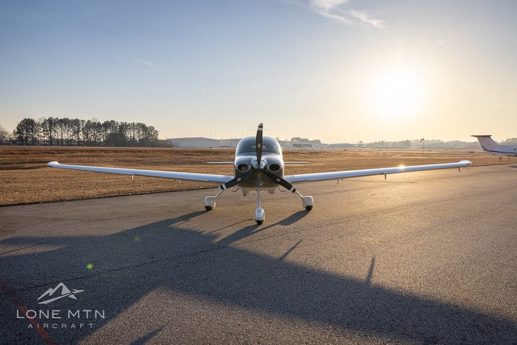 A Cirrus SR22T aircraft is parked on the tarmac with the sun setting in the background.