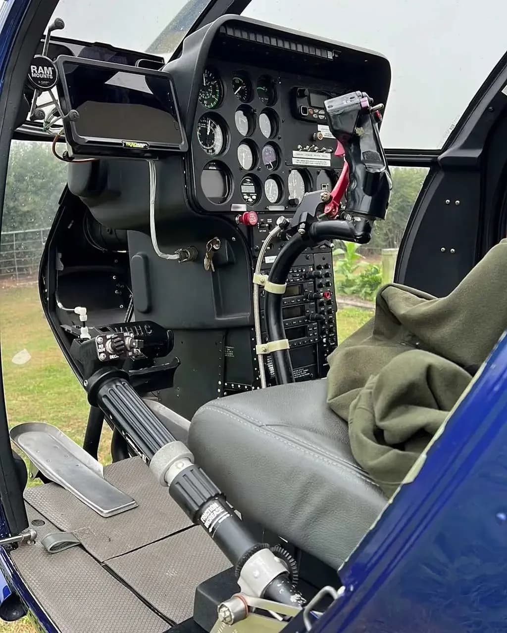 The cockpit of the MD 530 helicopter, showing the instrument panel, cyclic, collective, and a grey seat.