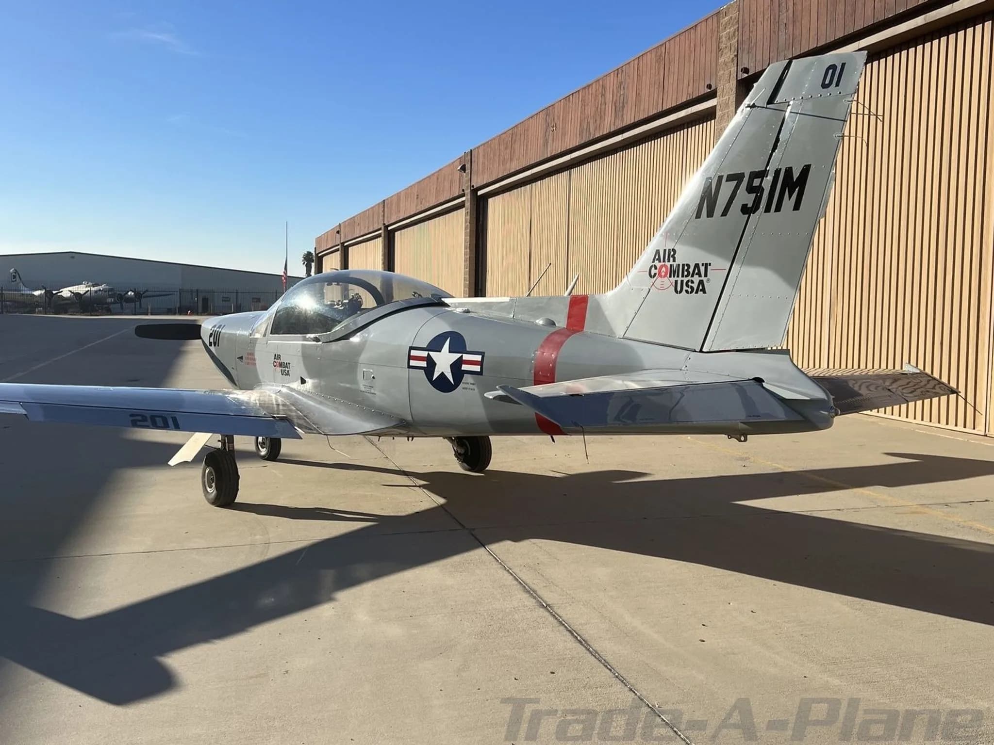 A rear-right view of the grey and red Air Combat USA aircraft 'N751M' showing the tail and US Air Force star insignia.