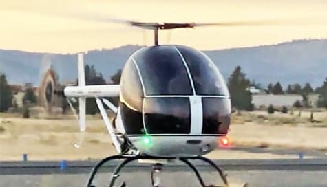 A white and blue helicopter sits on the runway with its lights on.