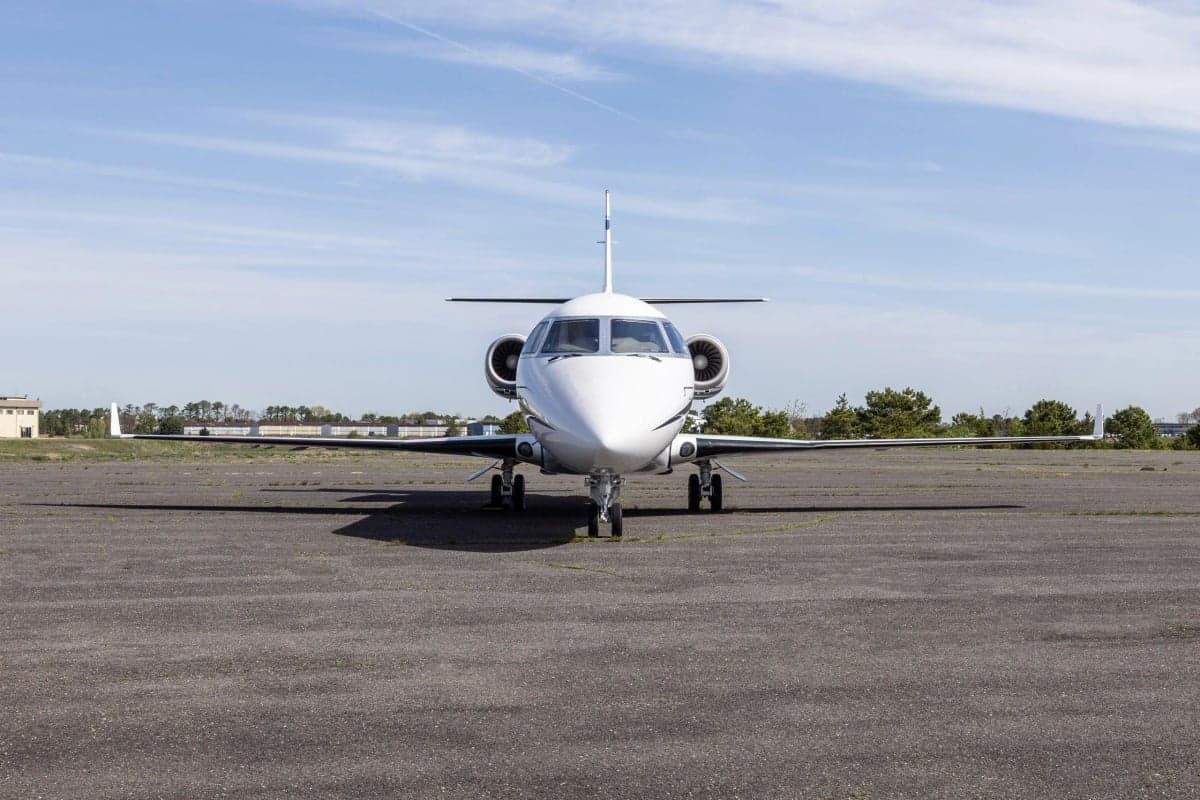 Front view of a white Gulfstream G150 aircraft with blue stripes parked on the tarmac.