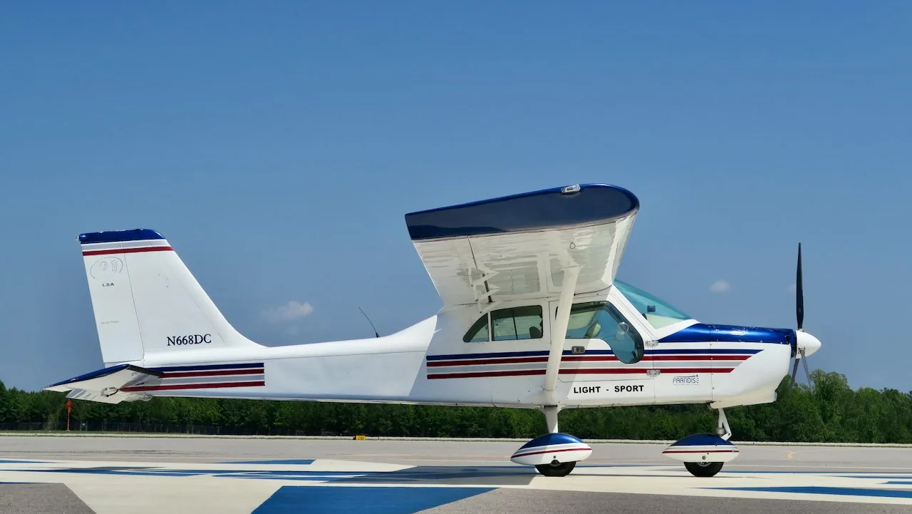A side view of a white Paradise P1 Light Sport aircraft with blue and red stripes, parked on a tarmac.