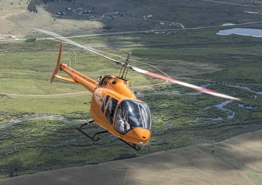 An orange helicopter flying over a green landscape.