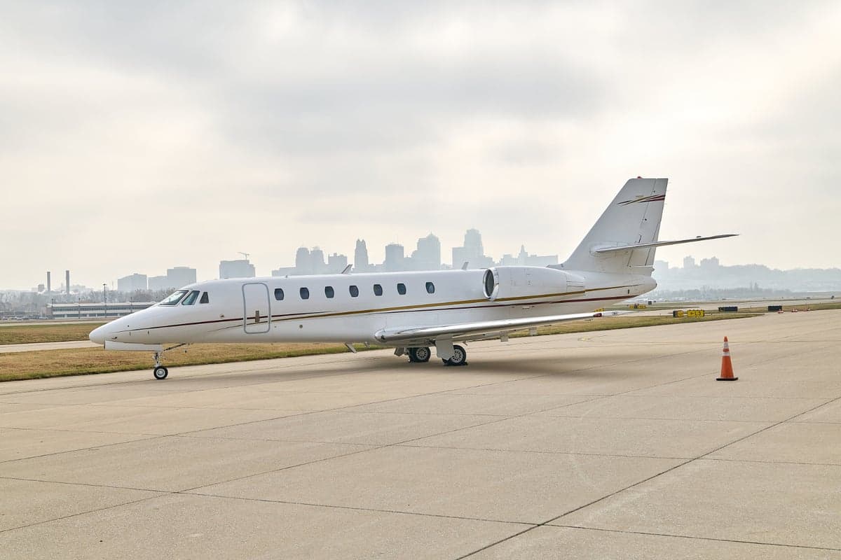 A white jet aircraft parked on the tarmac with a city skyline in the background.