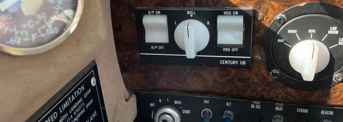 A close-up of an aircraft cockpit panel with wood grain, showing autopilot controls and other switches.