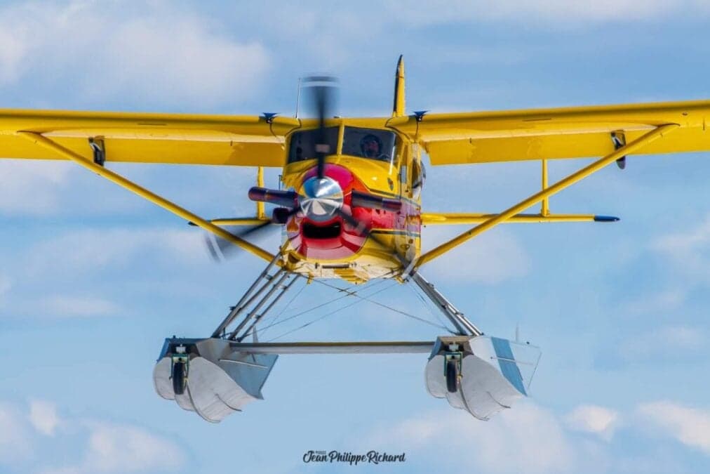 Front view of a yellow and red floatplane in flight against a blue sky.