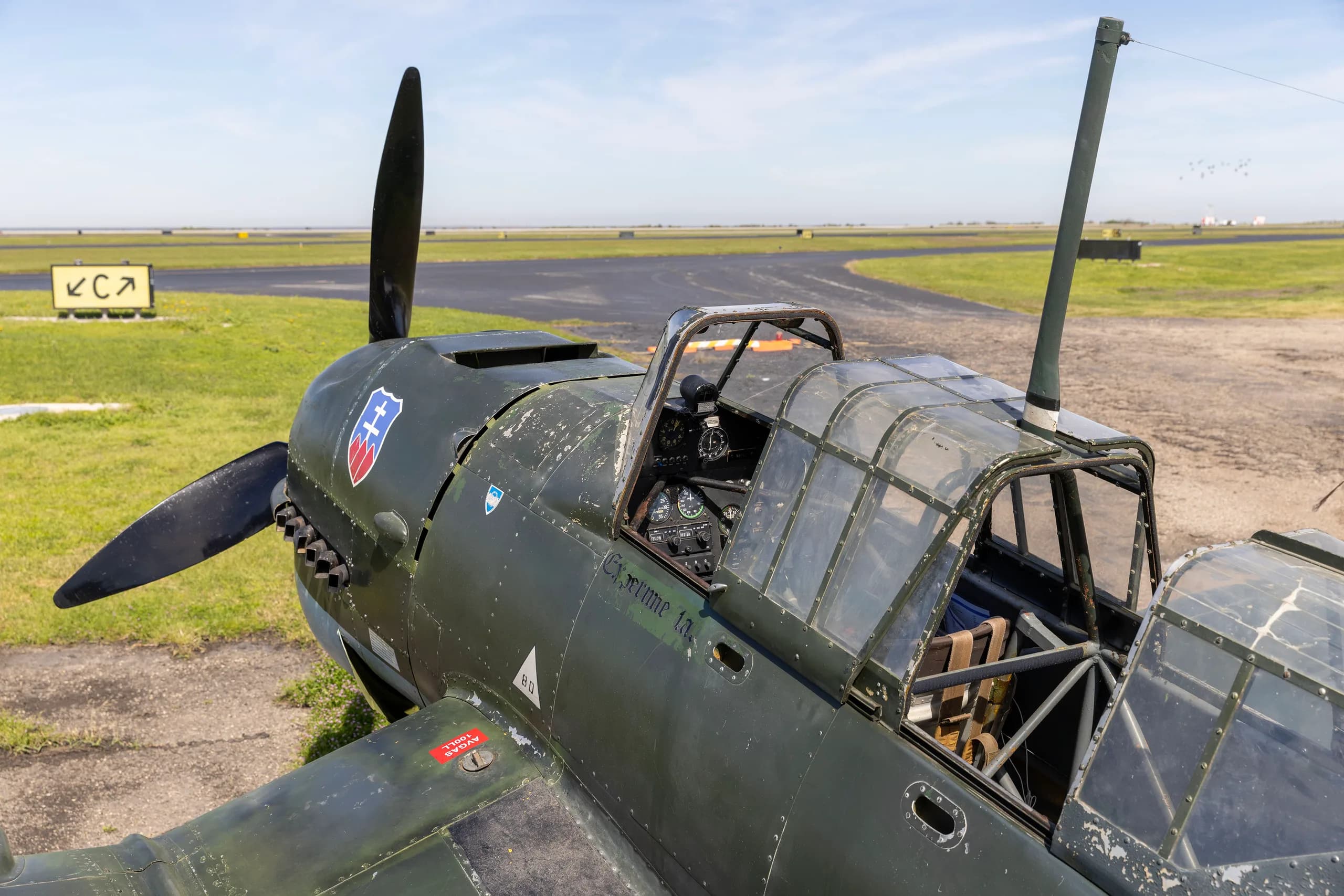 An overhead view of the front fuselage and open cockpit of a dark green Junkers Ju 87 Stuka on an airfield.