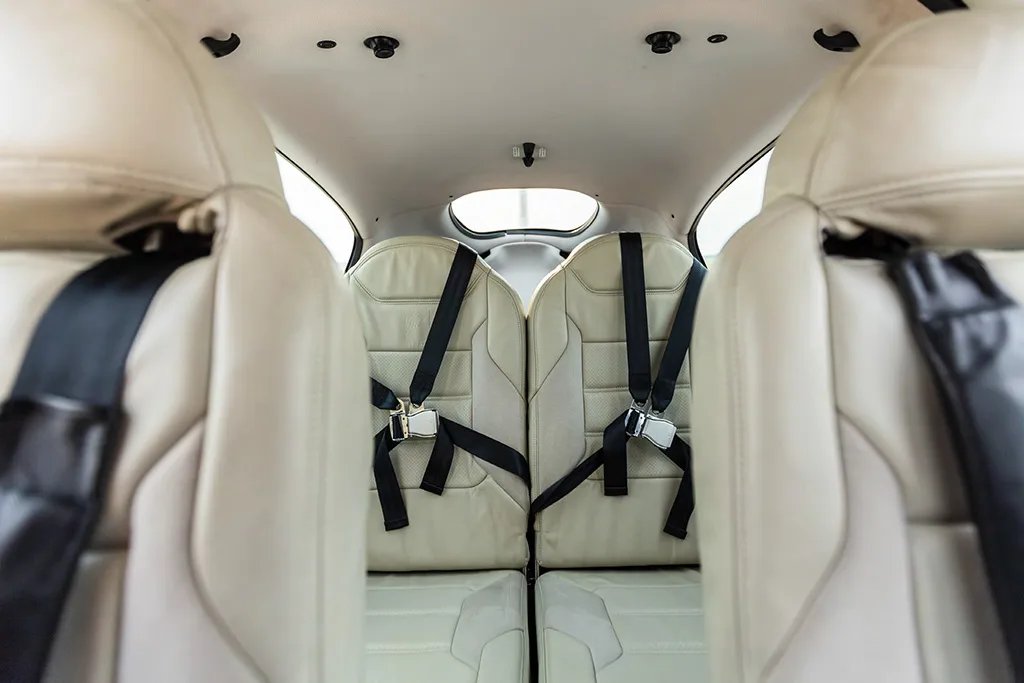 View of the light-colored rear passenger seats with harnesses in an aircraft cabin.