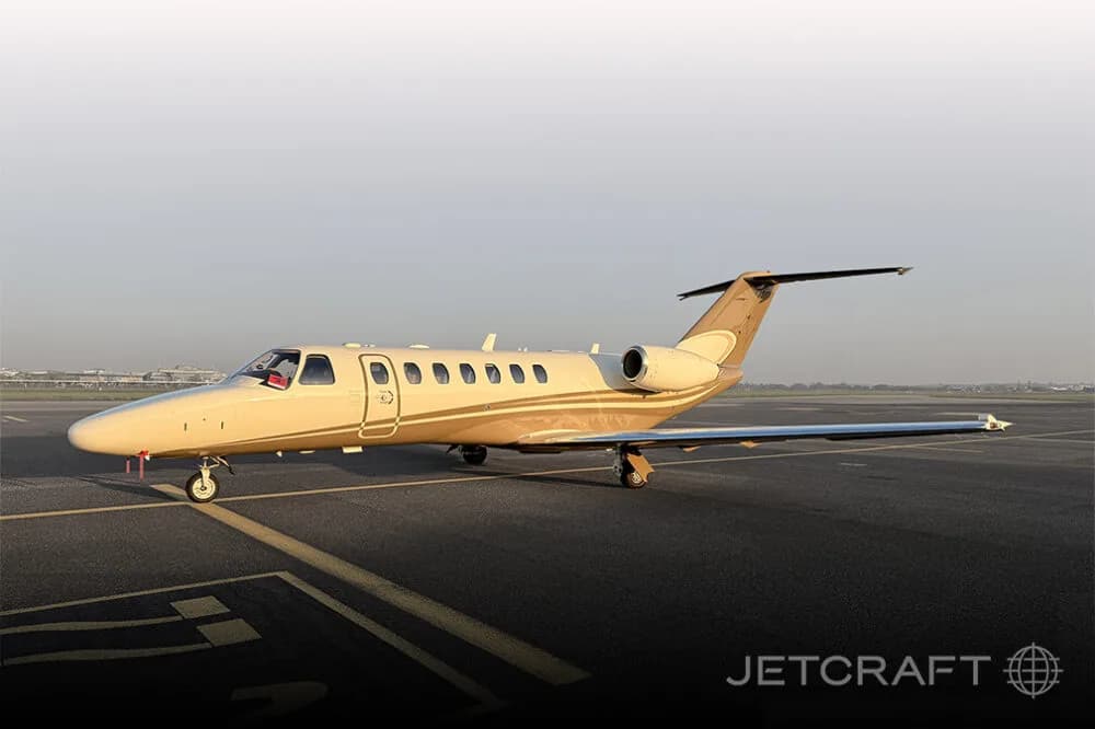 A beige and brown Cessna Citation business jet parked on an airport tarmac under a clear sky.