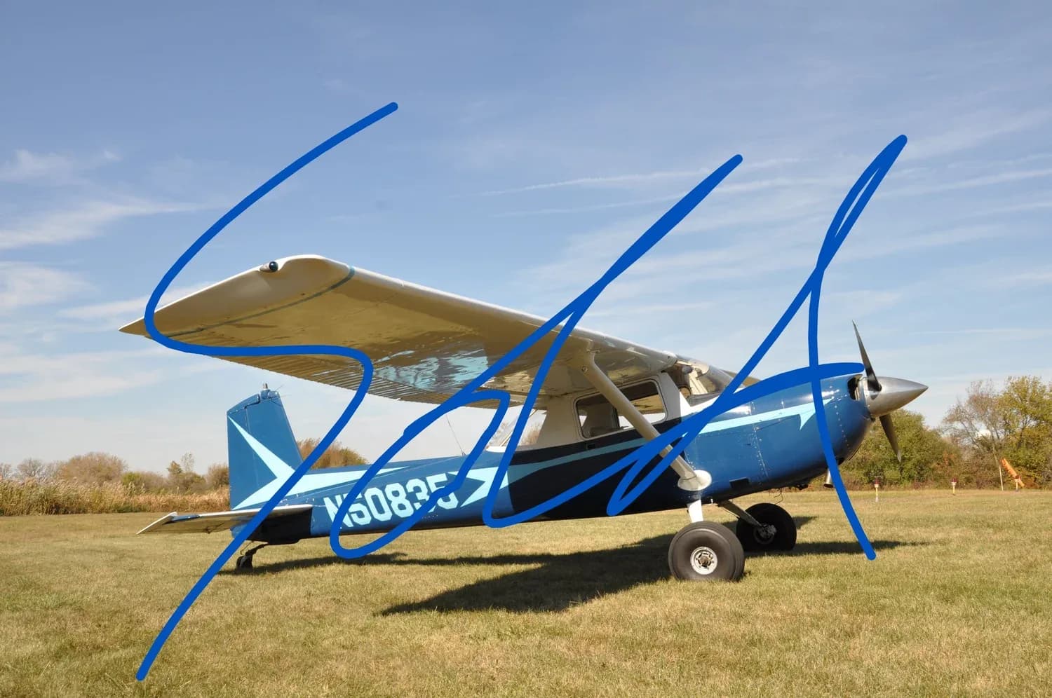 A blue and white Cessna-like single-engine aircraft, N5083F, is parked on a grassy field under a clear sky.
