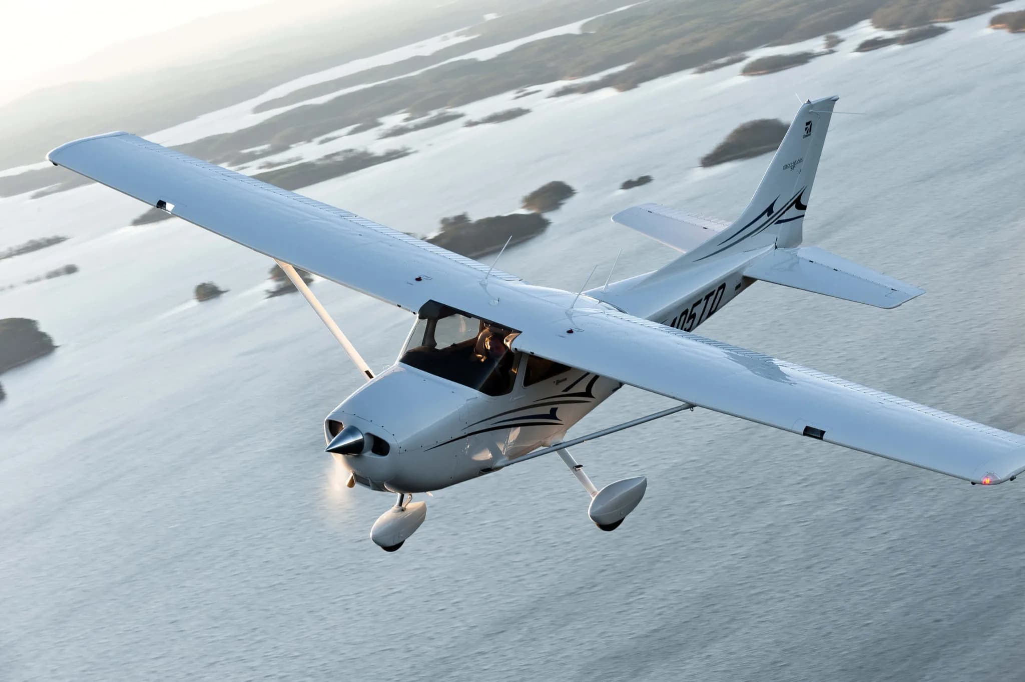 A Cessna 172 Skyhawk in flight over a body of water.