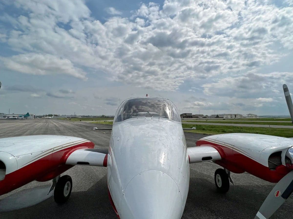 A head-on view of the white and red twin-engine aircraft N1242G on an airfield under a cloudy sky.