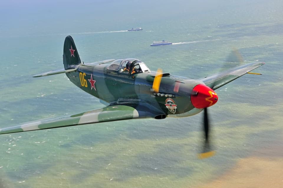Two Yak-3 aircraft in flight over farmland.