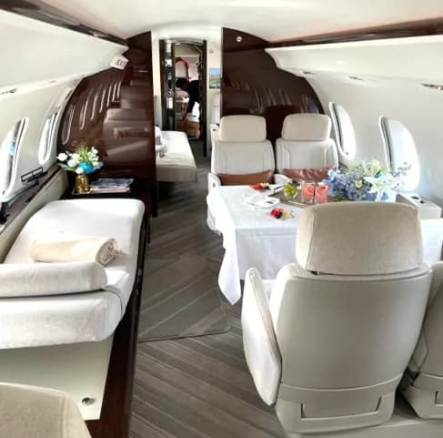 View of the aircraft interior with white leather seats, a table, and a bed.