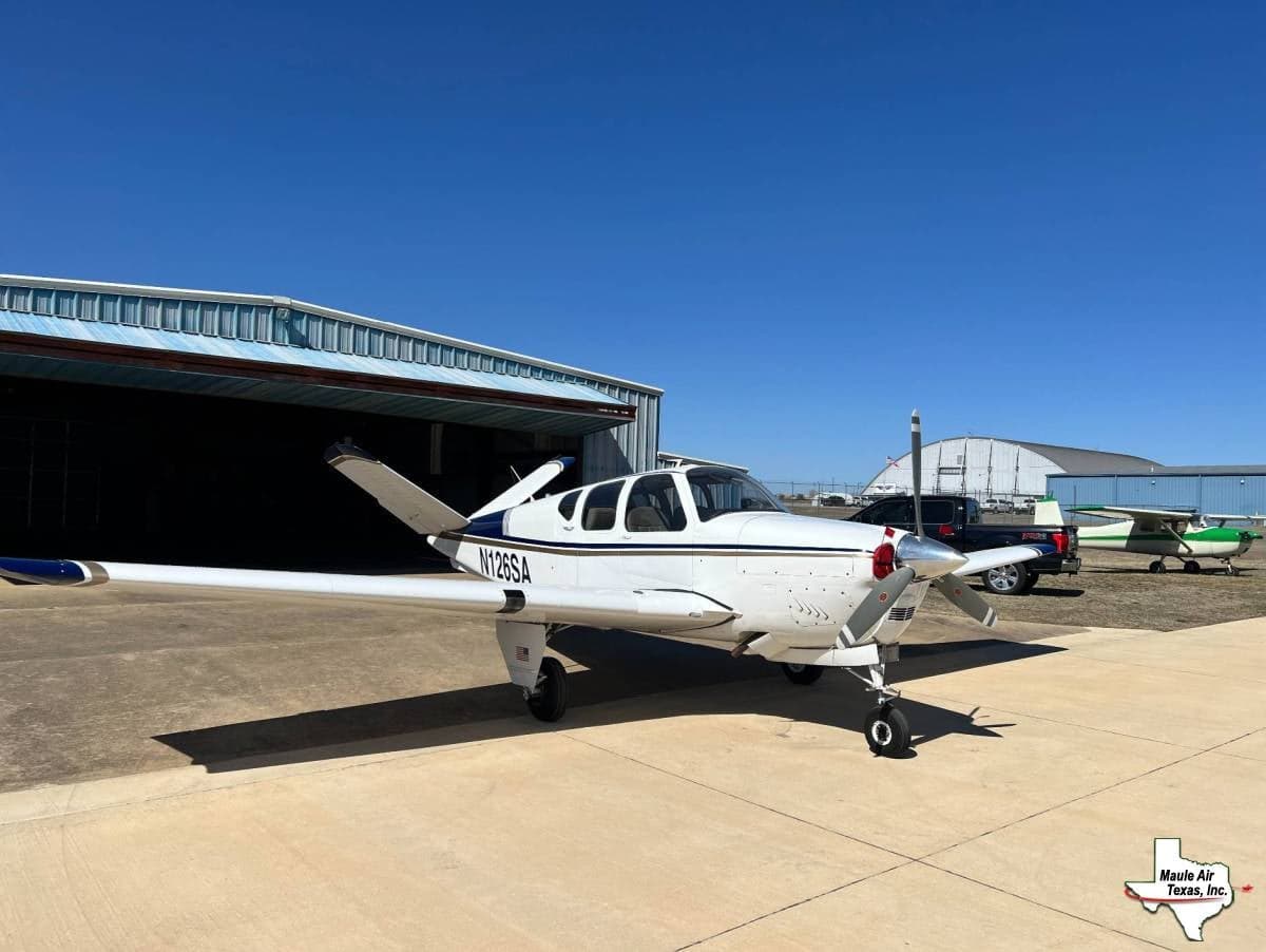 A white and blue Beechcraft Bonanza with tail number N126SA is parked on the tarmac.