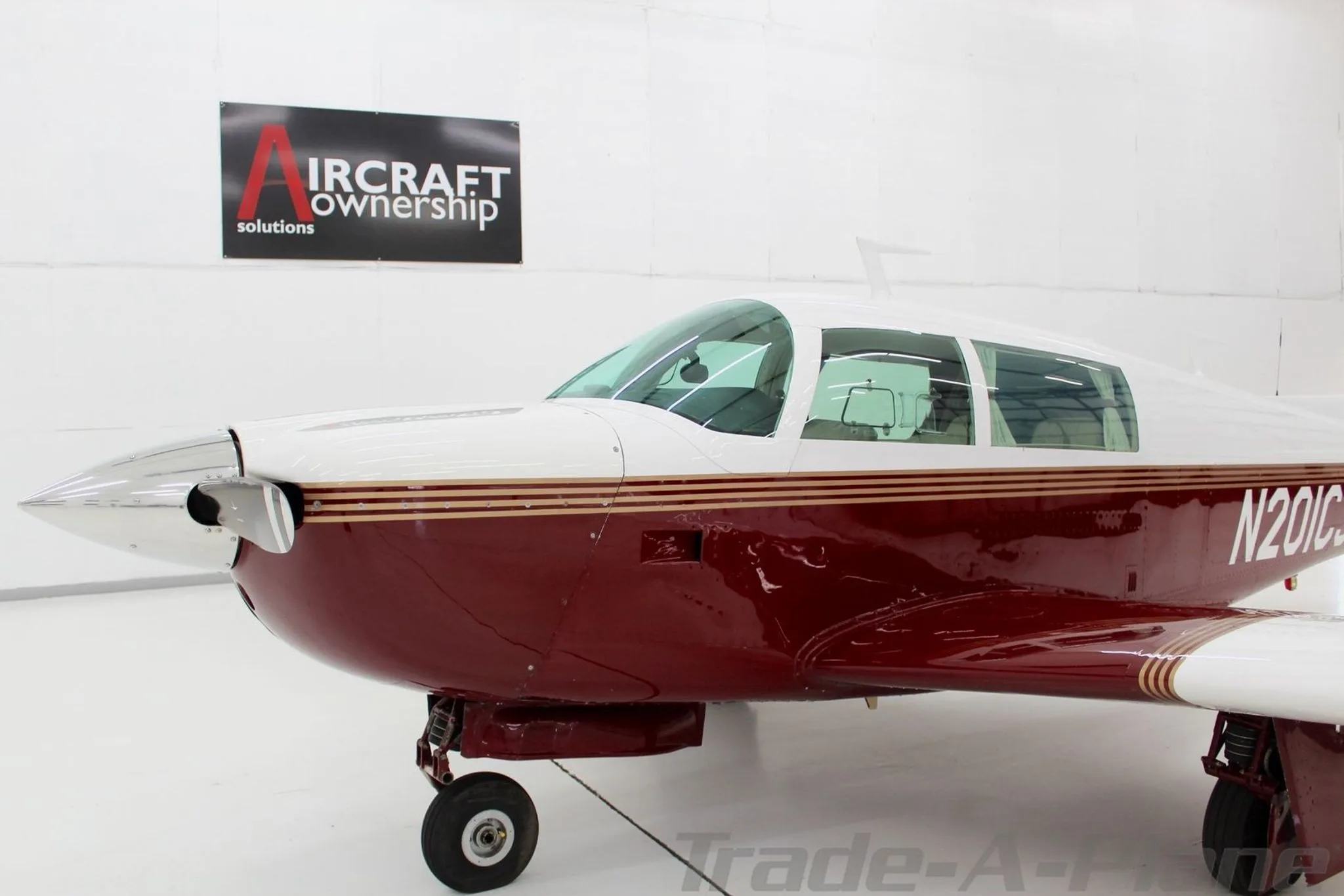 A close-up front-side view of the Mooney M20J aircraft, N201CJ, showing its propeller and cockpit windows.