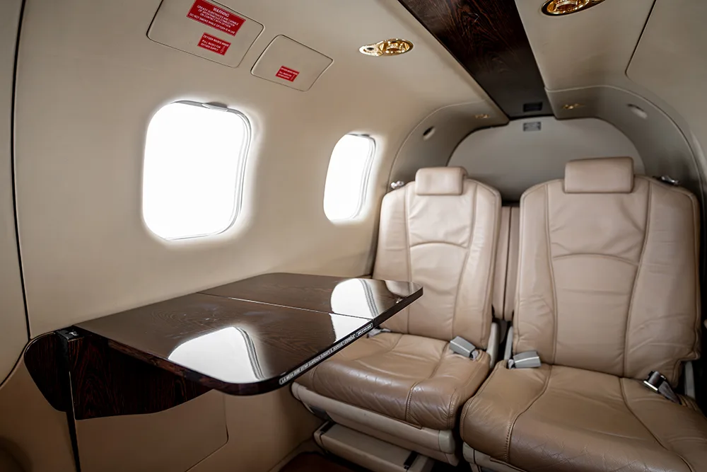 A close-up view of the aircraft cabin showing a fold-out table and two light beige leather seats.
