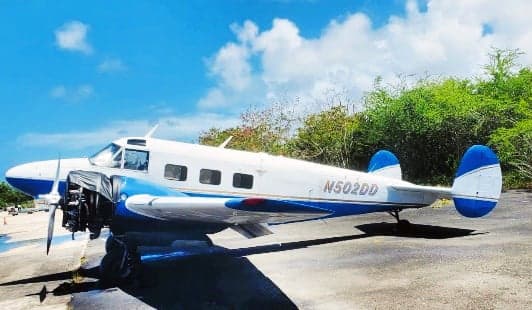 A Beechcraft Model 18 aircraft with blue and white paint scheme is parked on the tarmac.