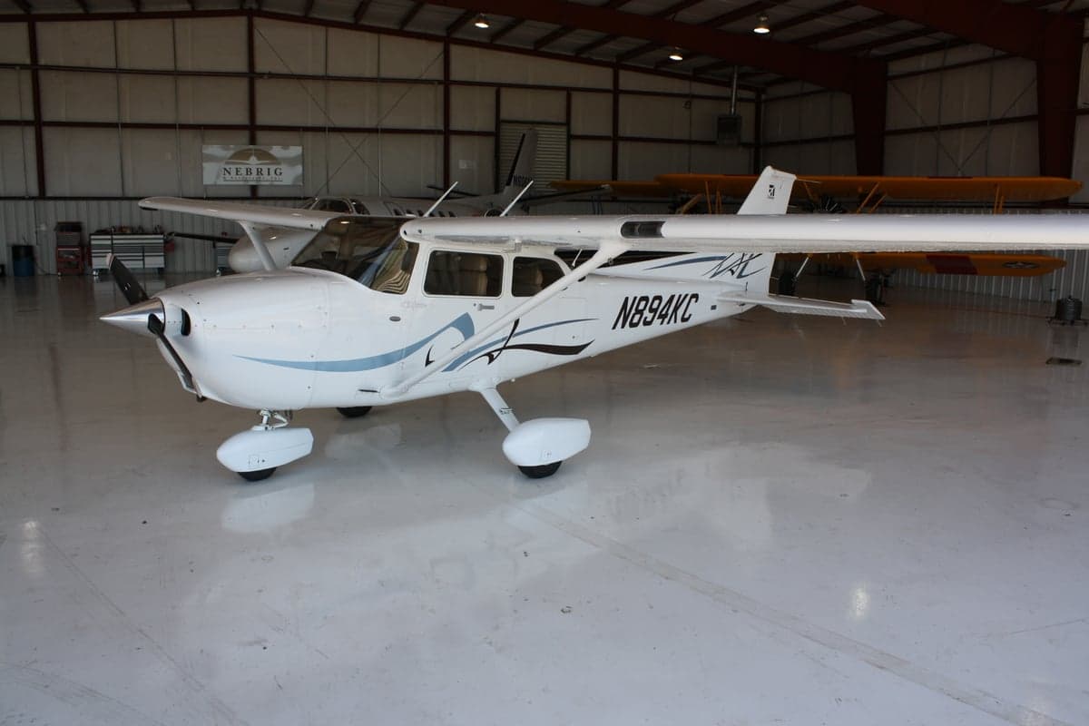 A white Cessna 172 aircraft with blue and black accents is parked in a hangar.