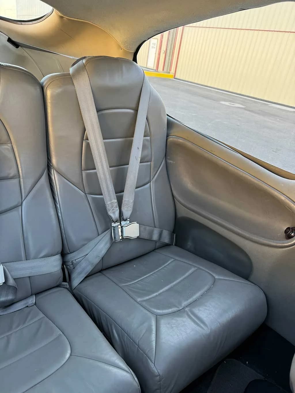A close-up view of a gray leather passenger seat with a seatbelt in the aircraft cabin.